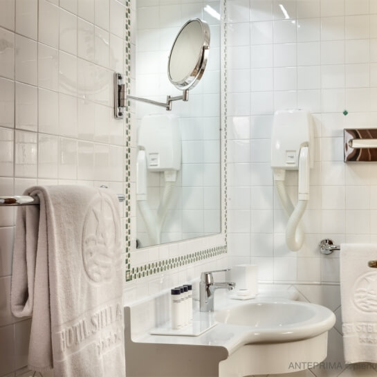 Bagno moderno con piastrelle bianche, lavabo, asciugamano, dispenser di sapone e porta asciugamani.