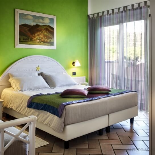 Camera da letto accogliente con parete verde, letto bianco, decorazioni artistiche e pavimento in piastrelle a spina di pesce.