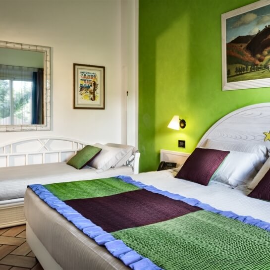 Chambre avec deux lits, mur vert, table de nuit entre les lits, décorations murales et ambiance accueillante.