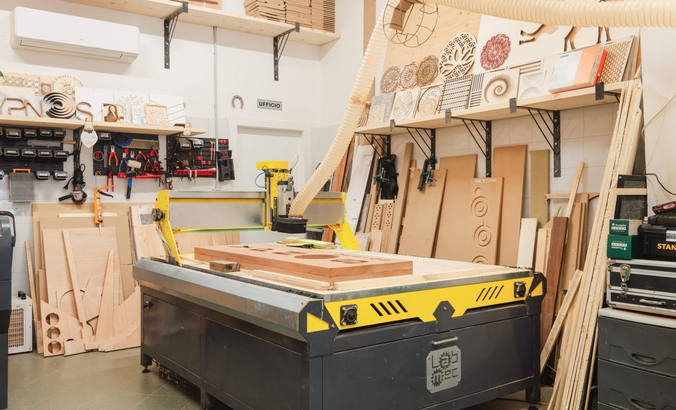 Laboratorio ben illuminato con attrezzature, un grande macchinario giallo e nero e oggetti in legno sparsi su un tavolo.